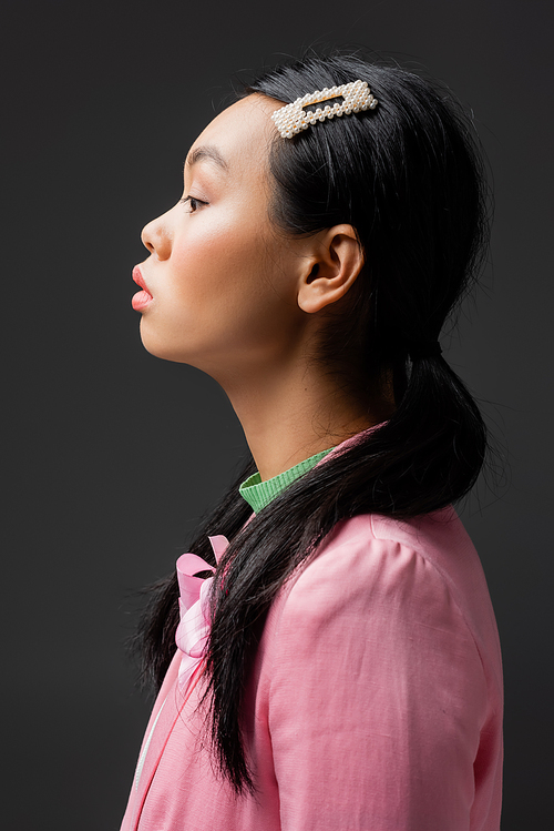 Side view of stylish asian woman with barrette on hair isolated on grey