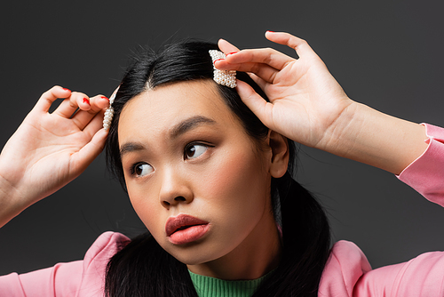 Pretty asian model touching barrettes and looking away isolated on grey