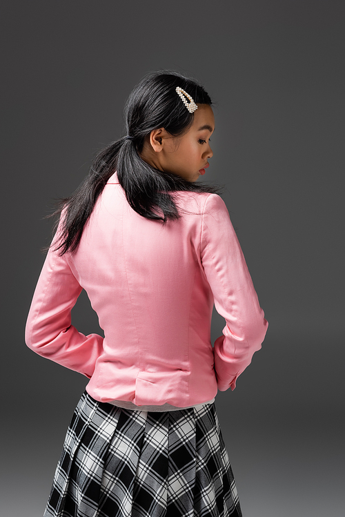 Side view of fashionable asian woman in plaid skirt and pink jacket isolated on grey