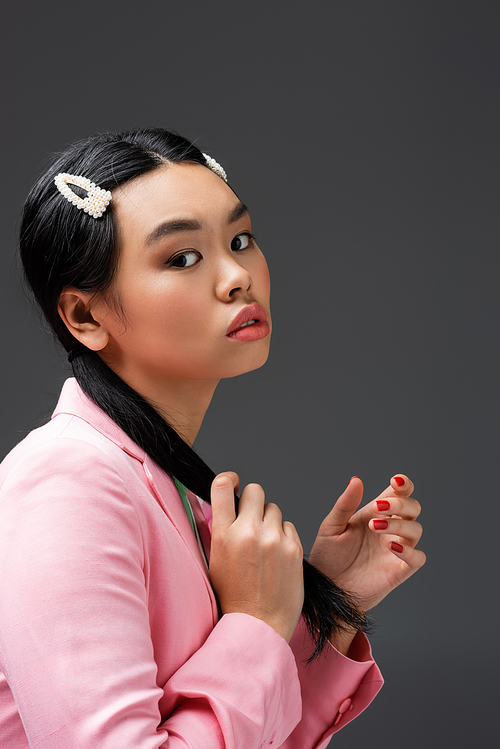 Portrait of asian woman in pink jacket touching hair isolated on grey