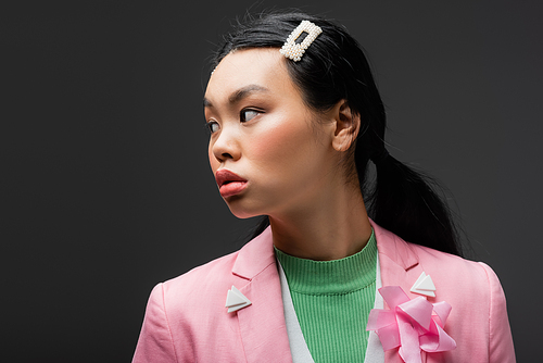 curious asian model in jacket looking away isolated on grey