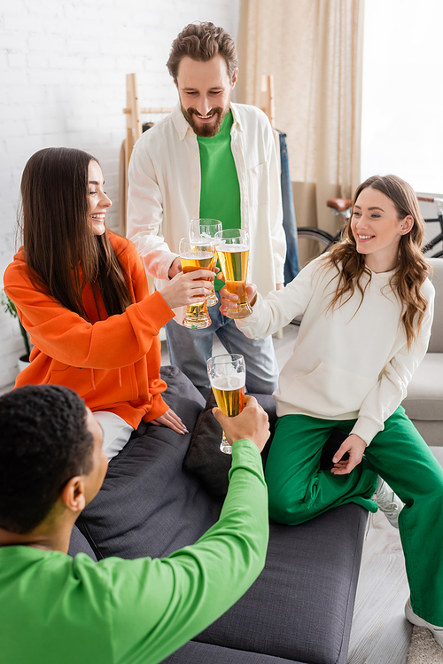 happy multiethnic friends toasting glasses of beer in living room