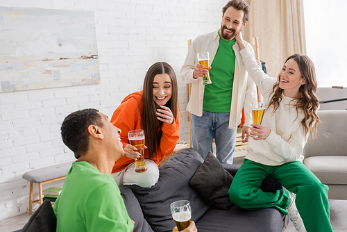 cheerful multiethnic friends holding glasses of beer while chatting in living room