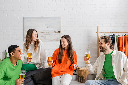 cheerful multiethnic friends holding glasses of beer while smiling in living room