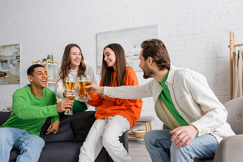 cheerful multiethnic friends clinking glasses of beer in living room