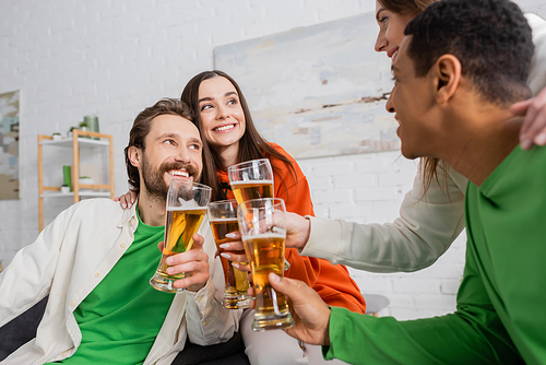 joyful and multicultural group of friends toasting glasses of beer in living room