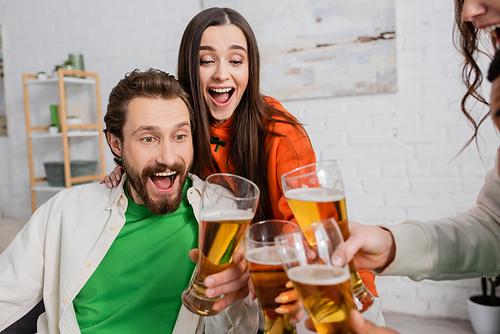 amazed group of friends toasting glasses of beer in living room