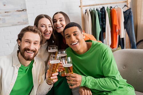 cheerful women and happy interracial men holding glasses of beer in living room