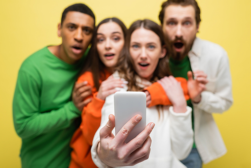 Blurred interracial friends using cellphone isolated on yellow