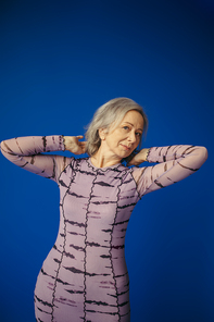 elderly woman in purple dress adjusting grey hair while posing on blue