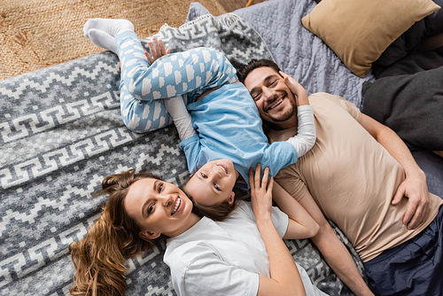 top view of positive parents and cheerful kid lying on bed at home