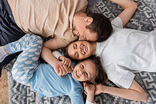 top view of pleased parents and cheerful kid lying on bed at home