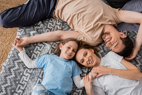 top view of joyful parents and positive daughter lying on bed at home