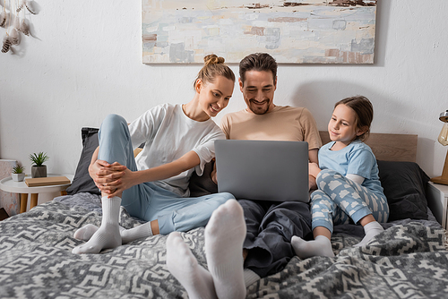 cheerful parents and happy kid watching movie on laptop in bedroom