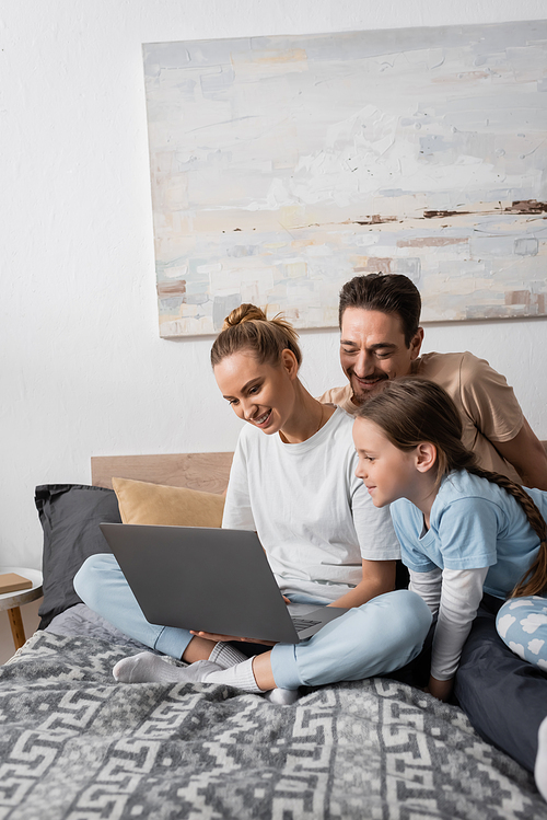 joyful parents and happy kid looking at laptop in bedroom