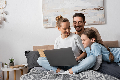 positive parents and happy kid looking at laptop in bedroom