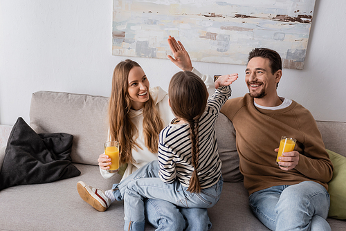 kid giving high five to cheerful mother near happy father sitting with glass of orange juice