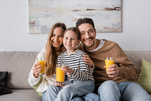 happy daughter sitting near positive parents holding glasses of orange juice