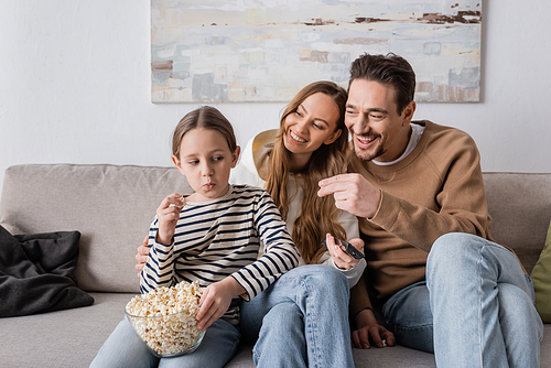 suspicious kid looking at father taking popcorn near cheerful mother with remote controller