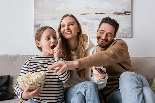 kid looking at happy father taking popcorn near cheerful mother with remote controller