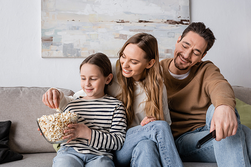 smiling kid looking at bowl while happy father taking popcorn near cheerful mother
