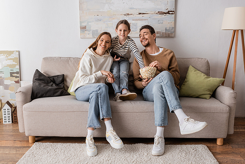 full length of happy kid with remote controller watching movie with cheerful parents