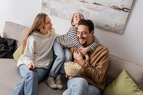 happy kid hugging bearded father with popcorn near smiling mother