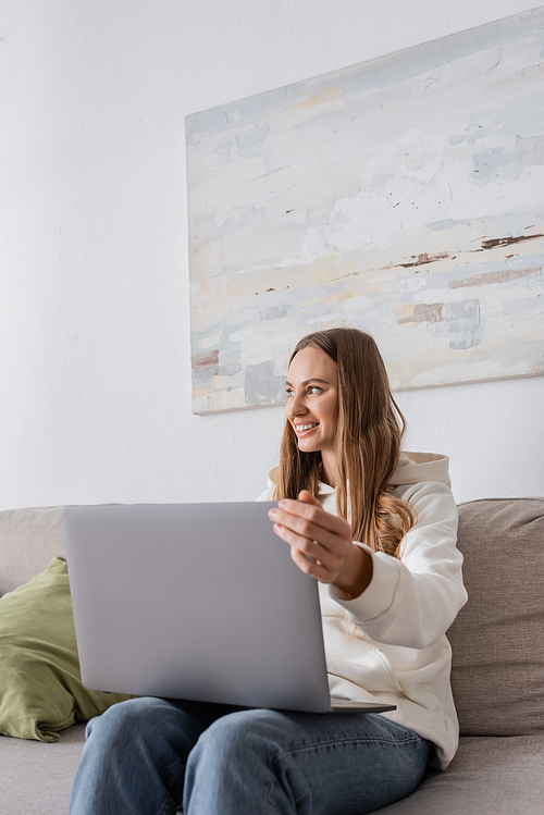 cheerful freelancer in casual clothes using laptop while sitting on couch