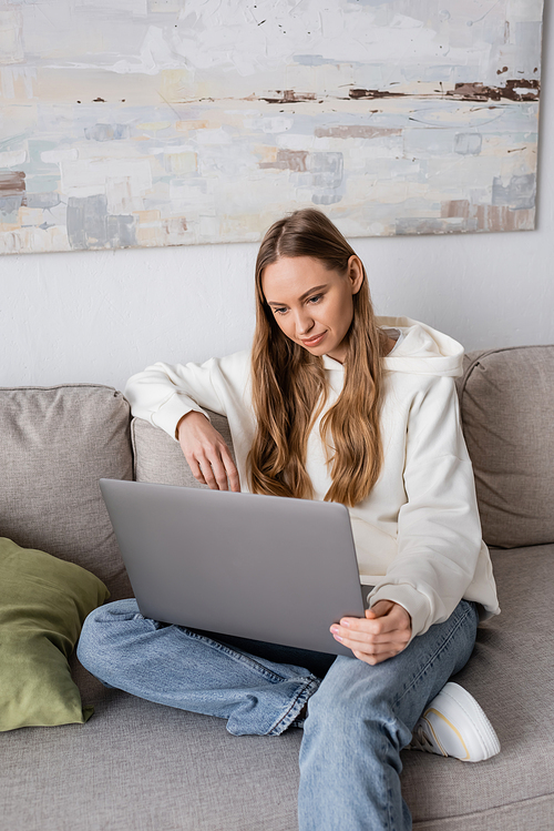 woman in casual clothes sitting on couch and using laptop in living room