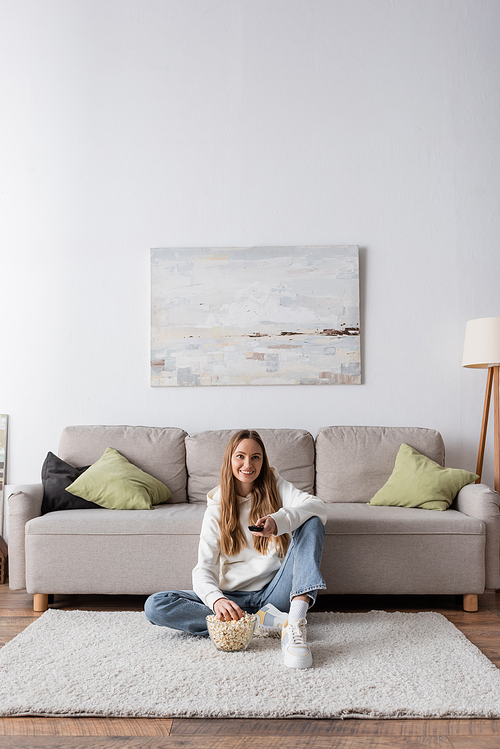 full length of cheerful woman holding remote controller while watching movie in living room