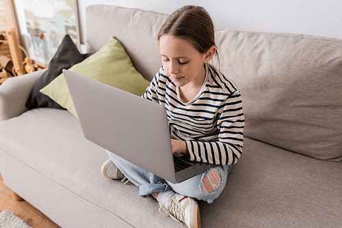 high angle view of preteen girl in casual clothes using laptop while sitting on couch
