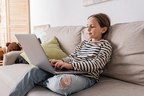 preteen girl in casual clothes using laptop while studying online and sitting on couch