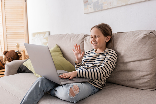 preteen girl in casual clothes having video call on laptop while sitting on couch