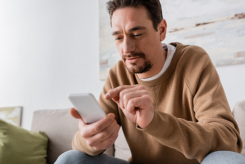 bearded man in beige jumper using smartphone at home
