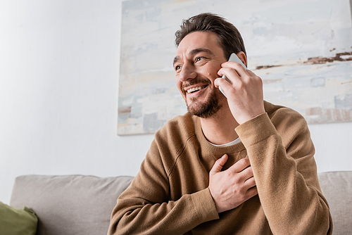 happy man in beige jumper talking on smartphone at home