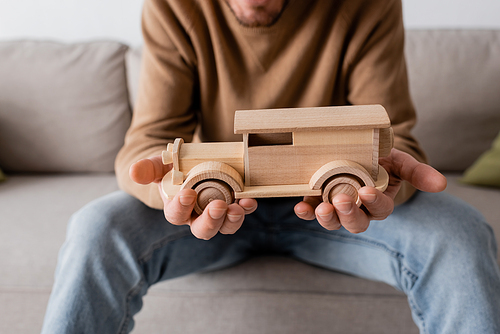 cropped view of bearded man holding wooden car toy in living room
