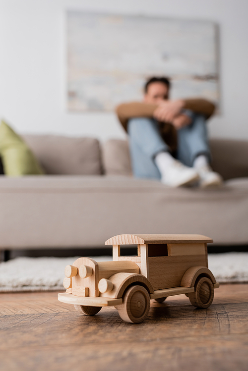 wooden car toy near blurred man sitting on couch in living room