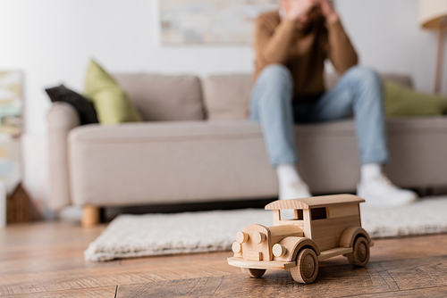 wooden toy vehicle near cropped blurred man sitting on couch in living room