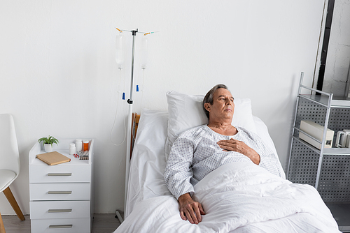 Elderly man lying near intravenous therapy in hospital ward