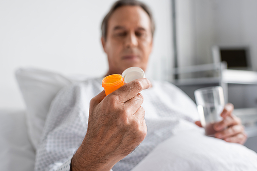 Blurred senior patient holding pills and glass of water in hospital ward