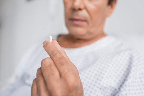 Cropped view of blurred senior patient holding pill in hospital ward
