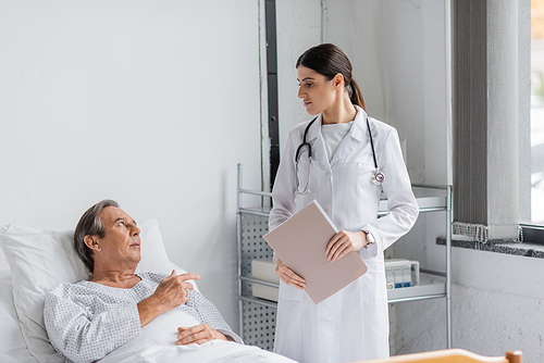 Sick elderly patient talking to doctor with paper folder in hospital