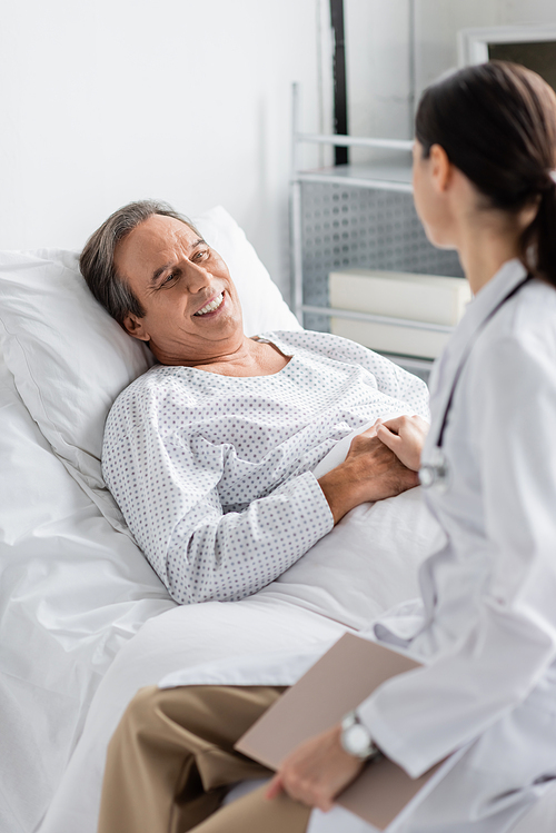 Blurred doctor holding hand of smiling senior patient in clinic