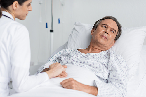 Blurred doctor touching hand of upset patient in hospital ward