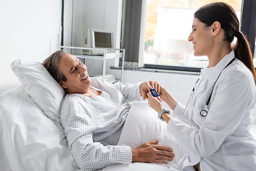 Positive doctor wearing pulse oximeter on finger of senior patient in hospital ward