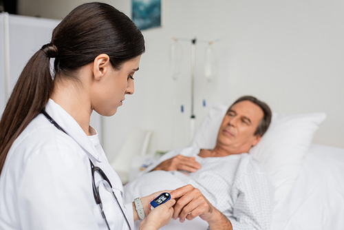 doctor looking at pulse oximeter on finger of senior patient in hospital