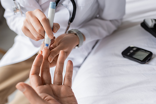 Cropped view of doctor with lancet pen checking blood sugar of patient in clinic