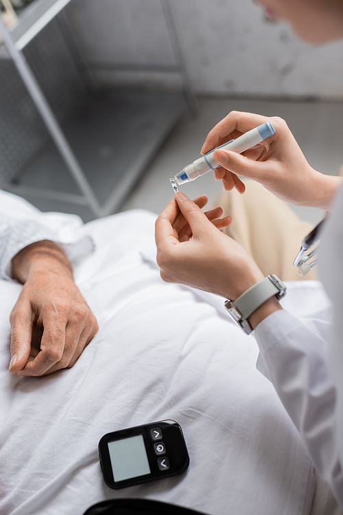 Cropped view of doctor holding lancet pen and test strip near glucometer and patient in clinic