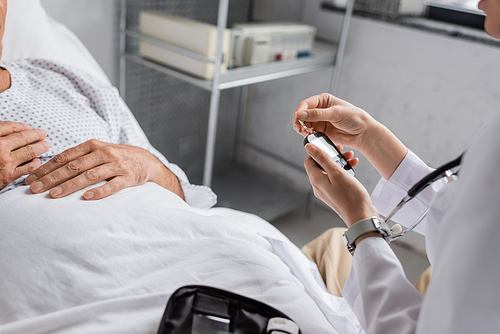 Cropped view of doctor holding glucometer near elderly patient in clinic