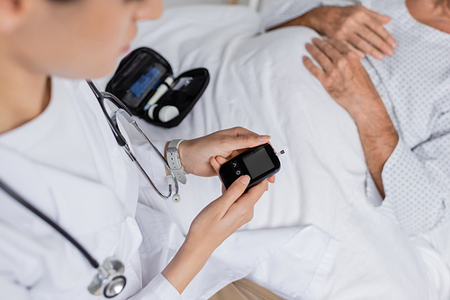 Cropped view of doctor holding glucometer near sick senior patient in hospital